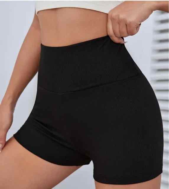 Close-up of black invisible shapewear shorts, highlighting the high waist and ribbed texture, worn by a woman in a minimalistic setting.